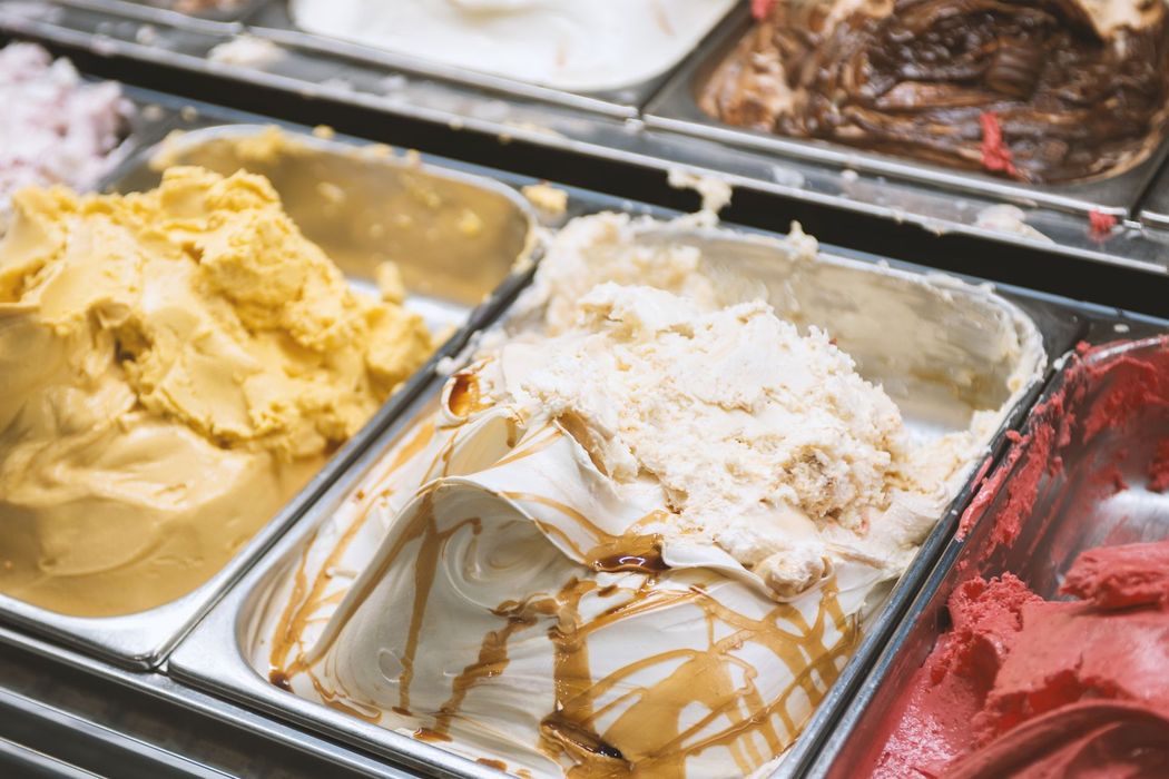 Assortimento di gusti di gelato in una vetrina, tra cui caramello, vaniglia, giallo, cioccolato e lampone.