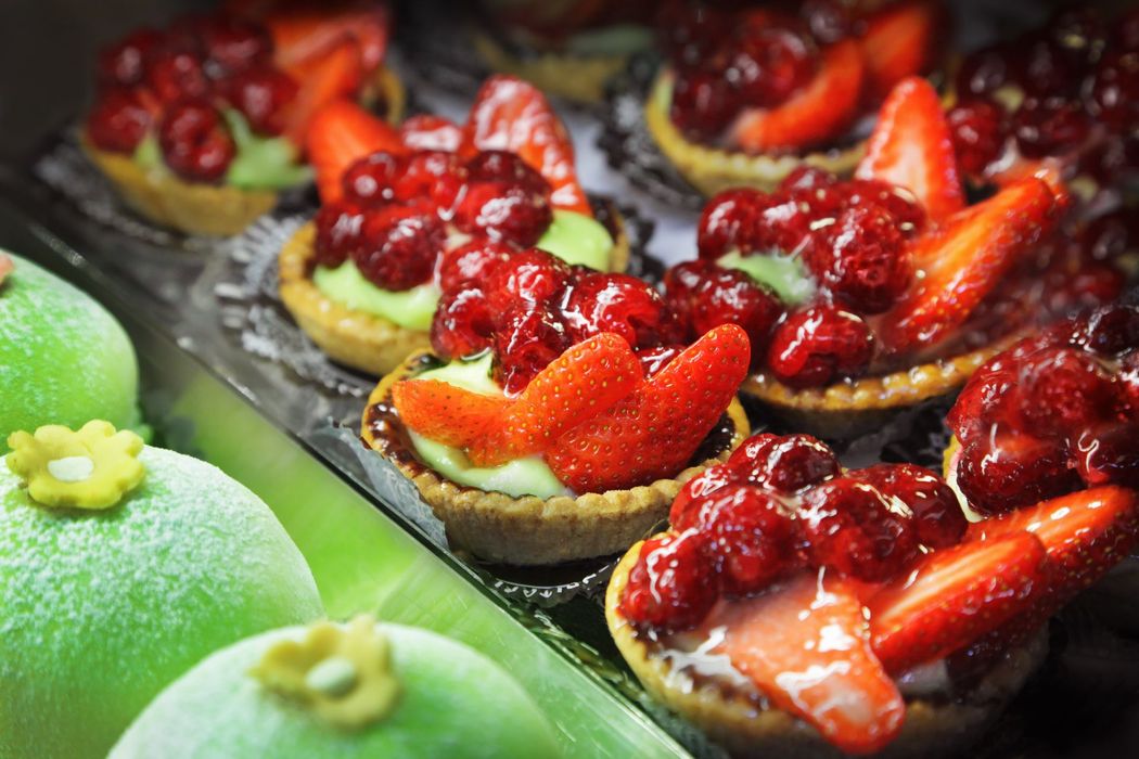 Crostatine assortite alla frutta, guarnite con fragole e frutti di bosco su un vassoio, accanto a dolcetti verdi ricoperti di zucchero