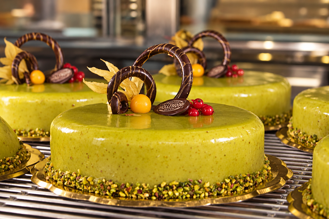 Dolcetti glassati di verde, decorati con anelli di cioccolato e frutti di bosco, su una griglia da pasticceria