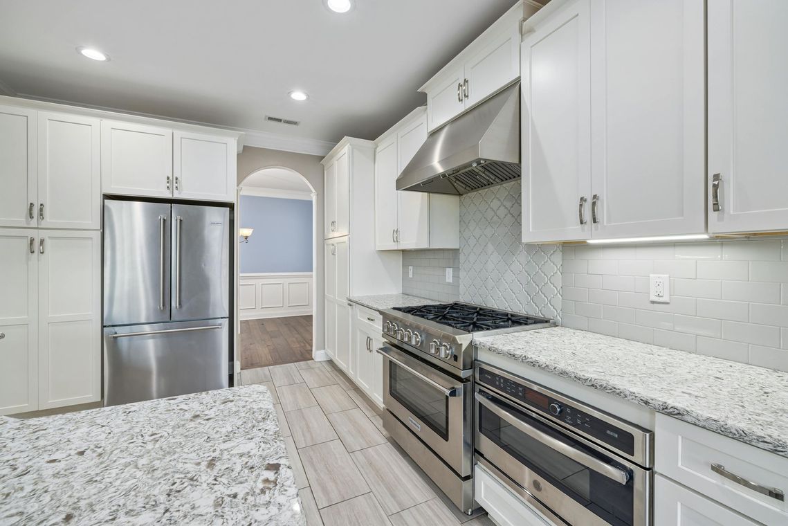 Bright modern kitchen with white cabinets, stainless steel appliances, and speckled granite countertops
