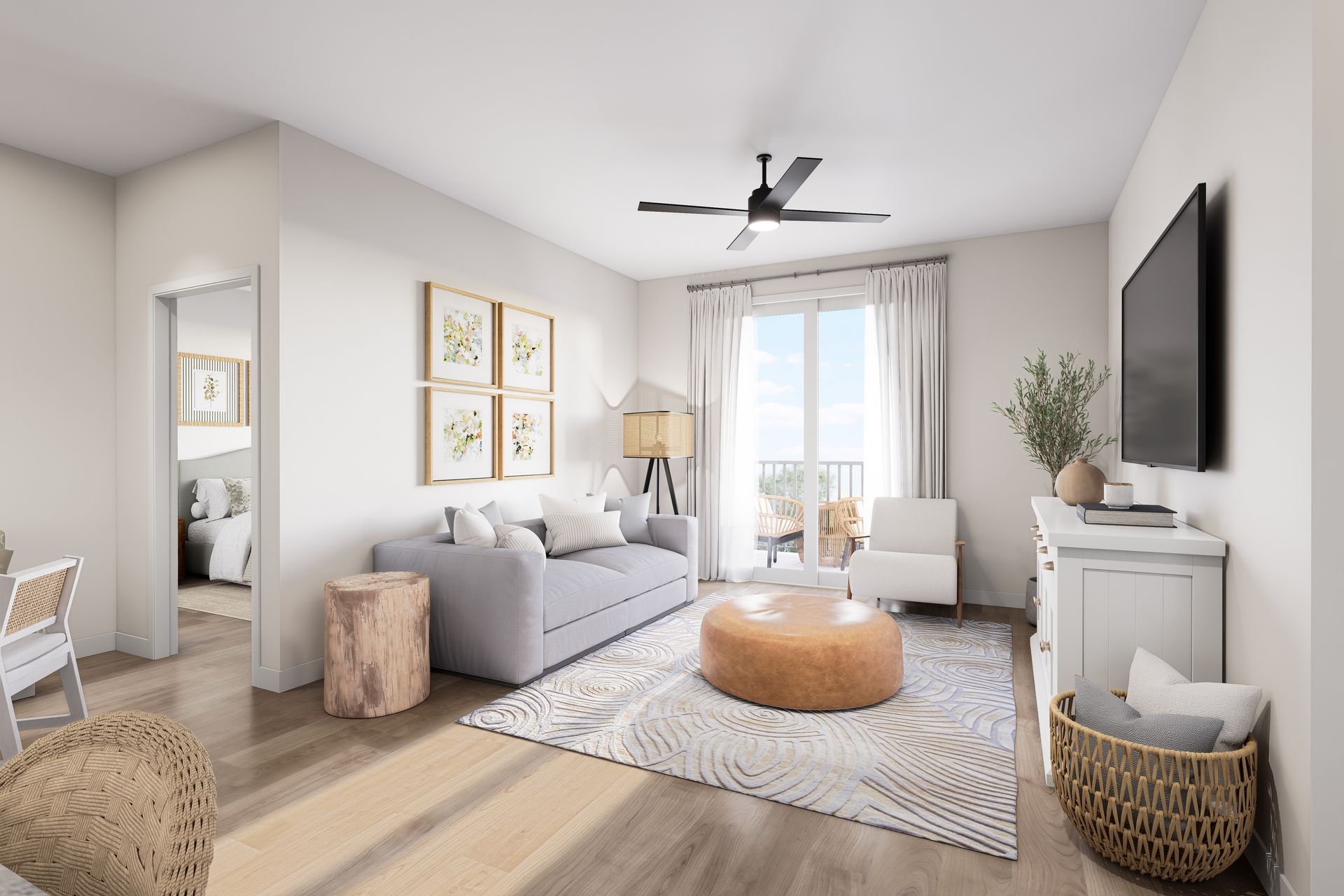 Bright living room with gray sofa, round ottoman, wall-mounted TV, and large window with sheer curtains.