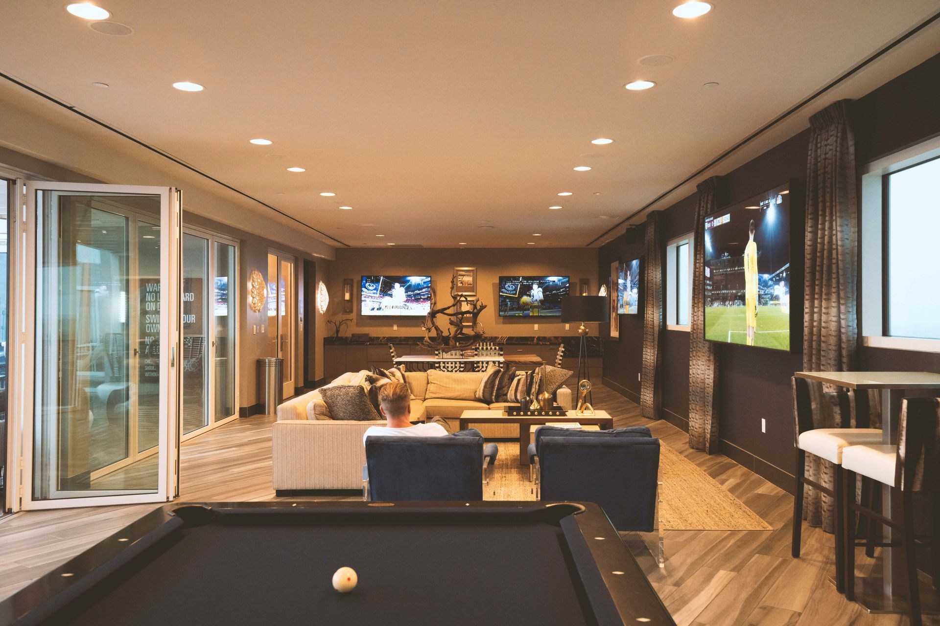 Modern lounge with pool table, sofas, TV, and large windows overlooking a scenic outdoor view