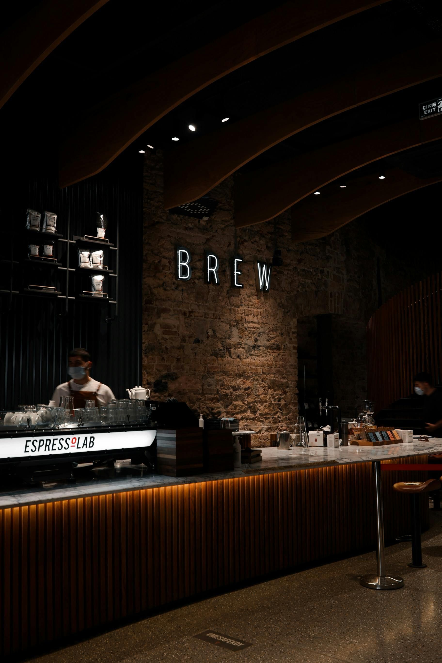 Dimly lit modern café bar with brick wall, curved ceiling, and a barista behind the counter.