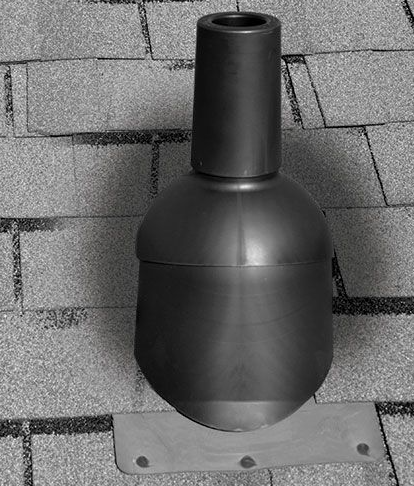 Worker installing gutter on a brick wall beside gray roof shingles, using a hand tool.