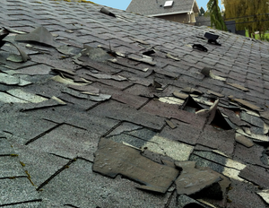 Damaged shingled roof with missing and torn sections near a roof vent