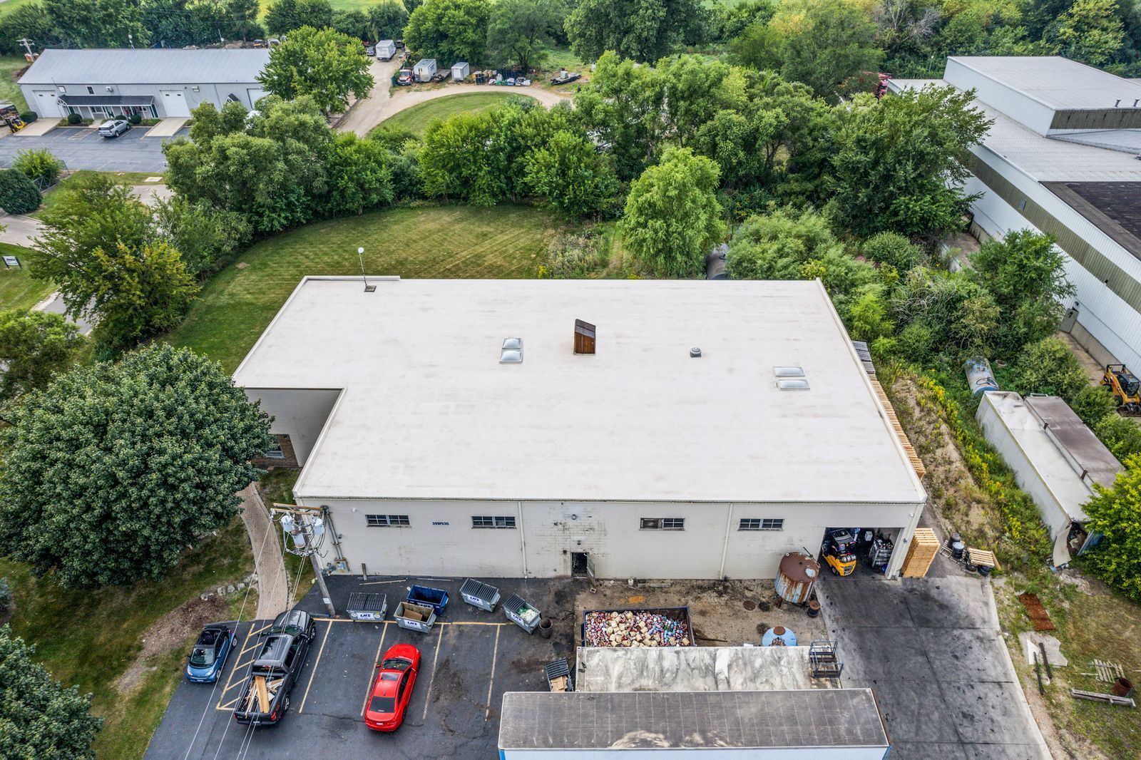 Aerial view of a white-roofed building with parked cars and trees around it.