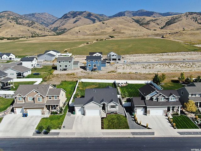 Sunlit rural valley with homes, green fields, and red cliffs under a clear sky