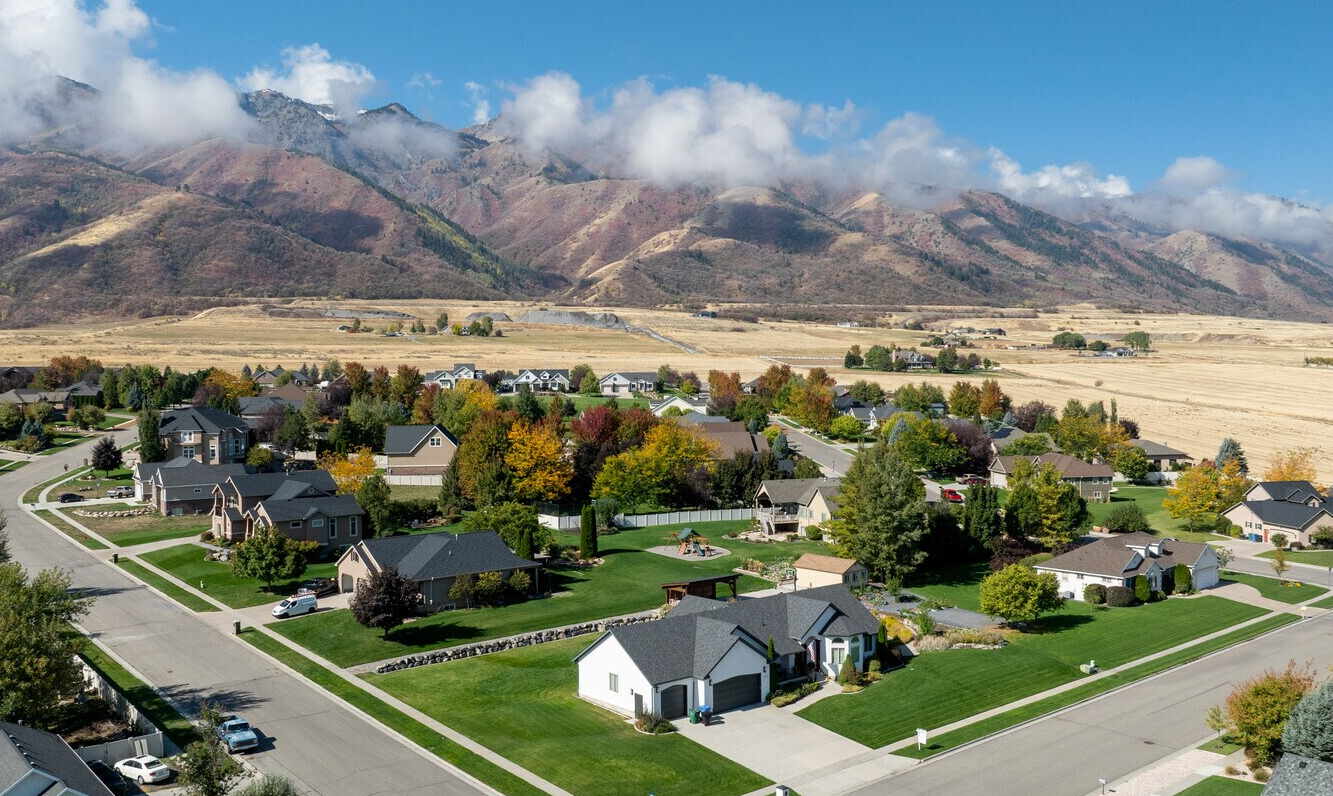 Desert suburb with tan homes, red rock cliffs, and blue sky under bright sun