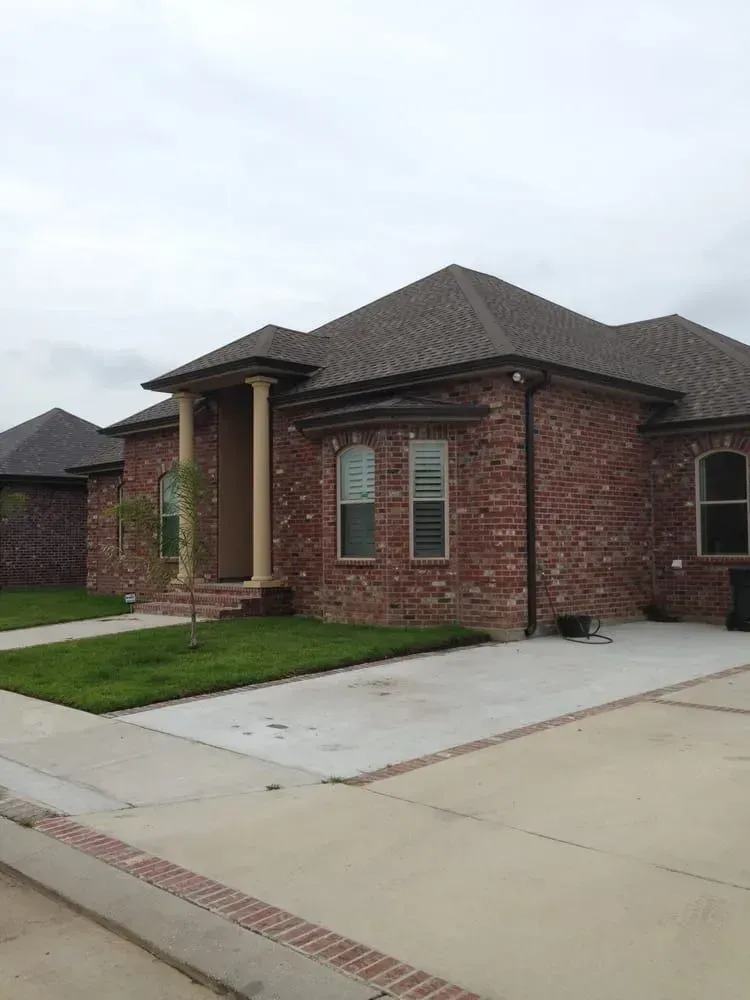 Brick house with concrete driveway, green lawn, and cloudy sky.