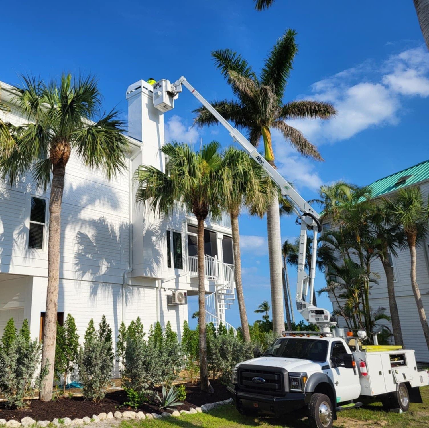 A white service truck with an extended boom lift reaches the chimney of a white house under a clear blue sky.