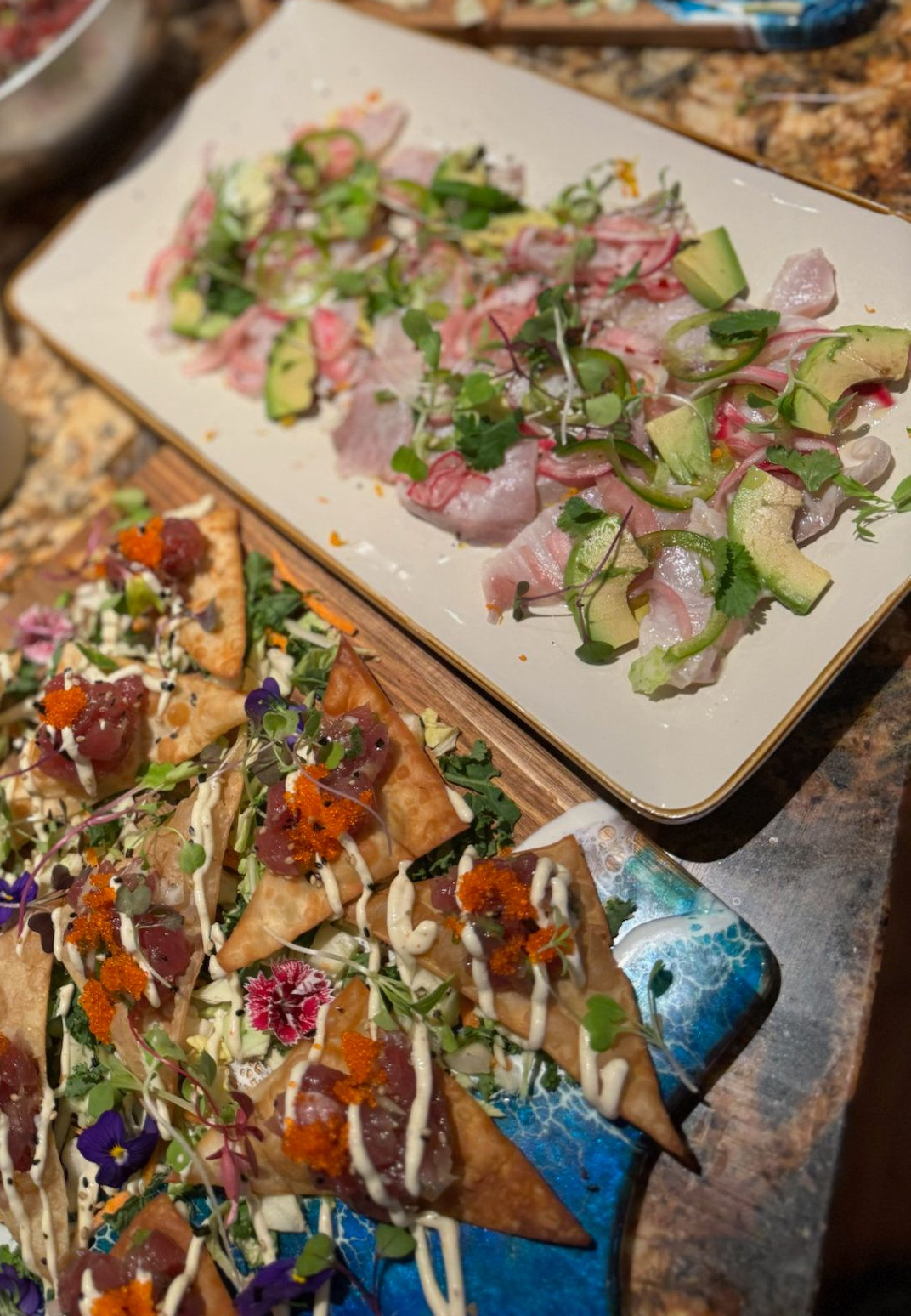 Plates of colorful sliced appetizers topped with herbs and drizzled sauce on a table