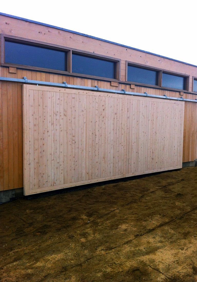 Tall wooden fence panels beside a beige building with blue windows on muddy ground