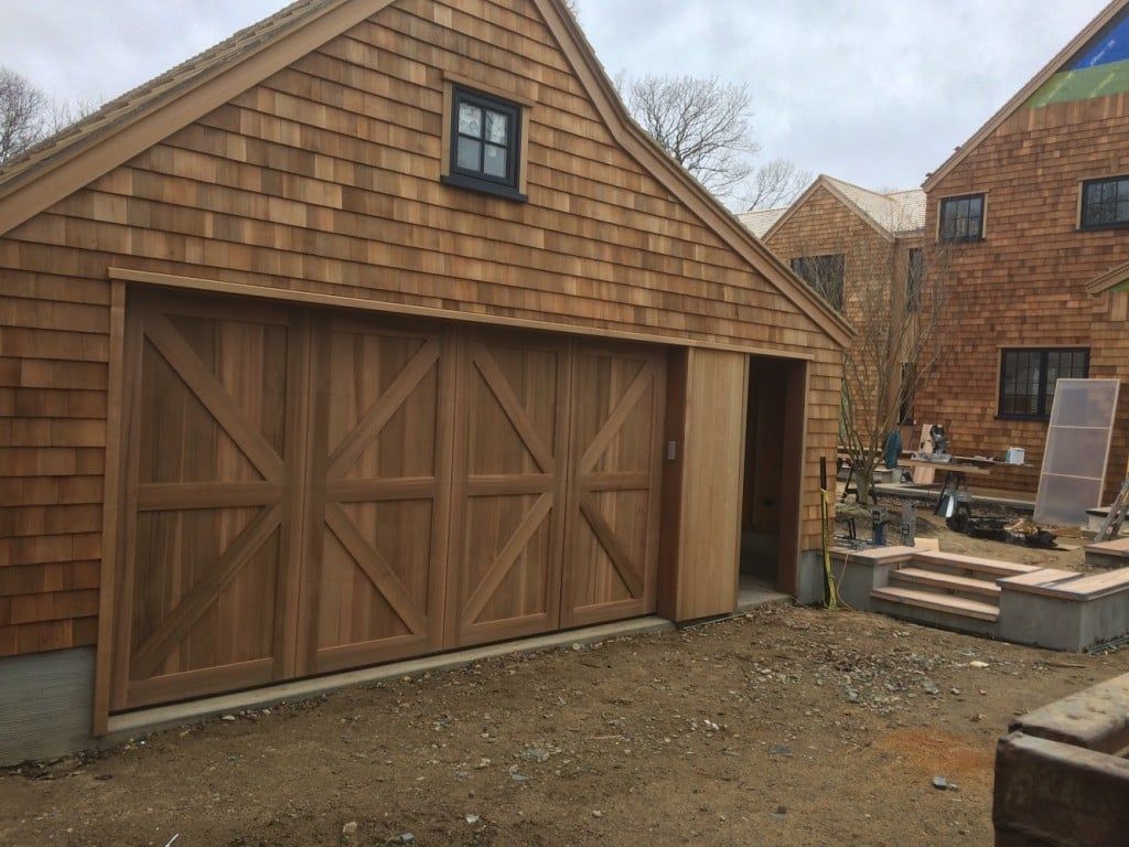 Wood-sided garage with barn-style double doors beside a house under construction