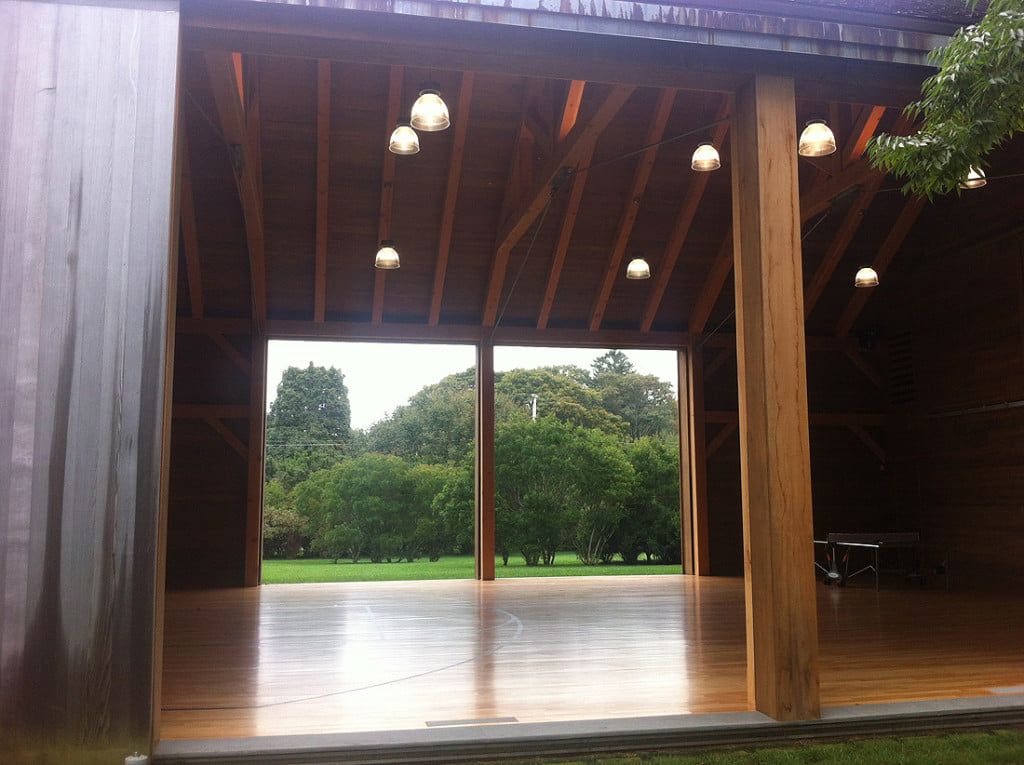 Open-air wooden pavilion with hanging lights, glossy floor, and green trees visible outside.