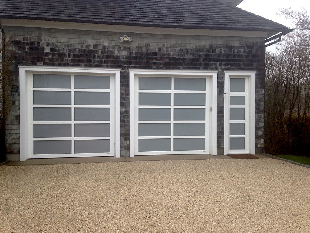 Three white garage doors on a stone house exterior with a gravel driveway