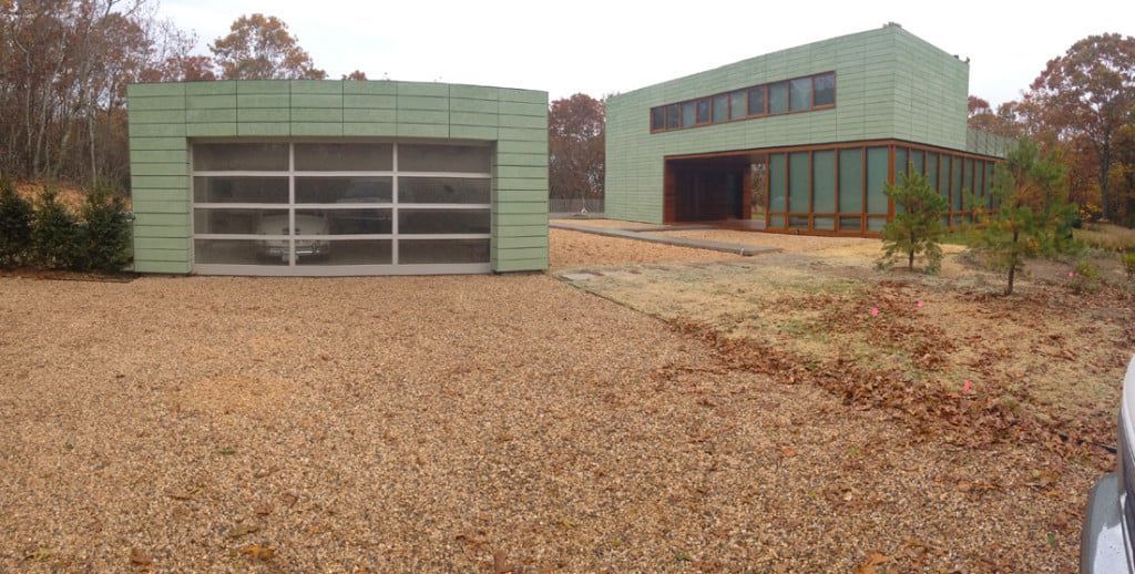 Two green buildings on a leaf-covered lot, one with a large garage door and one with windows.