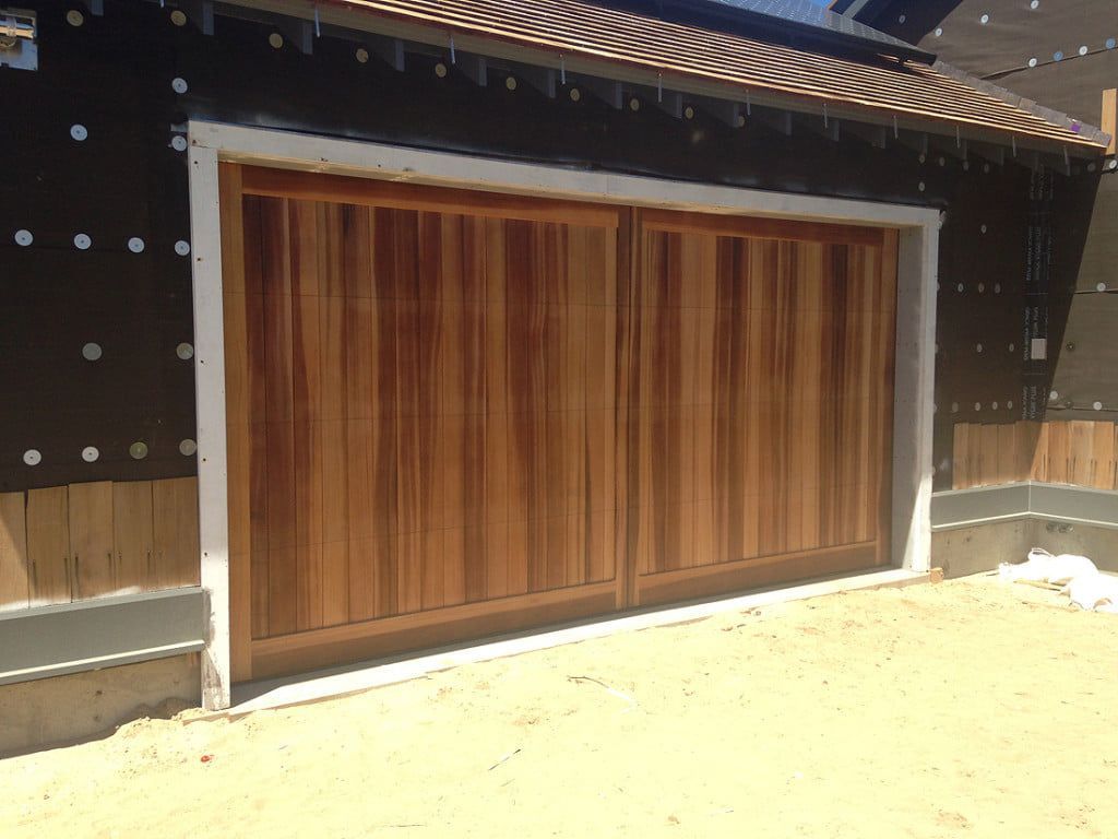 Wooden garage door set in a dark exterior wall, with a light concrete threshold.