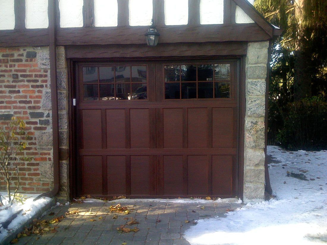 Wooden garage door on a stone-and-brick house, with snow on the ground.