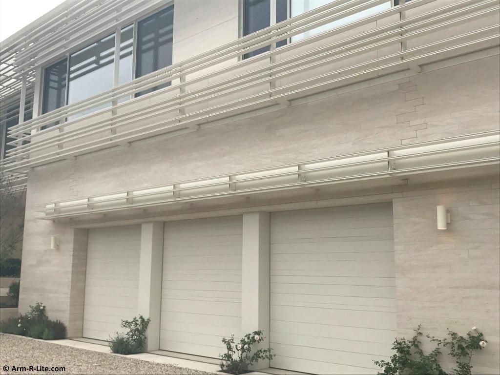Exterior of a building with three white garage doors and a balcony above them