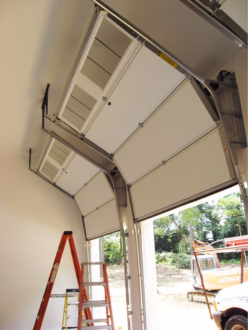 Interior view of a garage door under construction, with a red ladder and bright daylight outside.