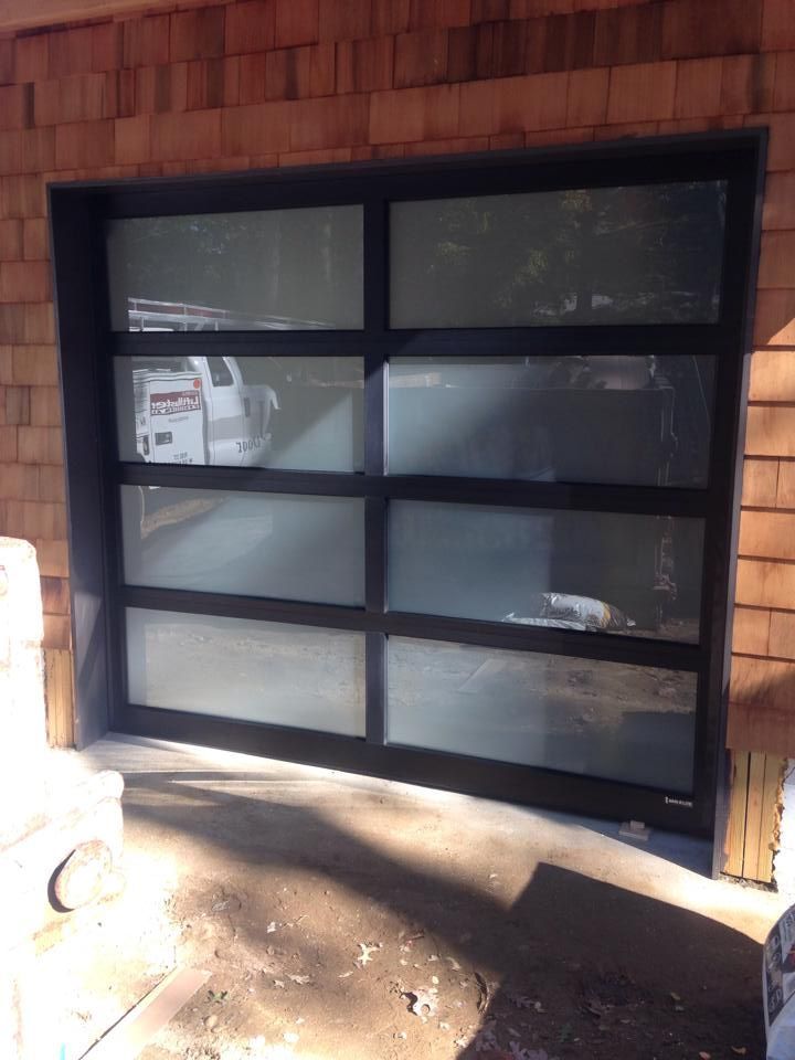 Black-framed frosted garage door with horizontal window panels in a brick wall, sunlight on the concrete.