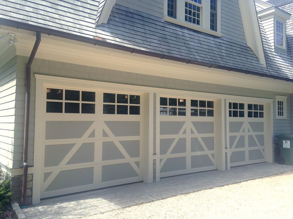 Three beige garage doors with white trim on a house exterior
