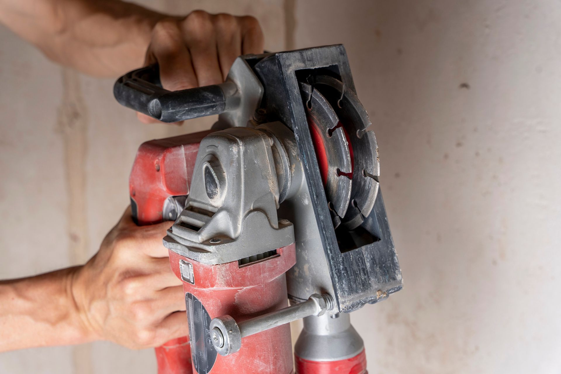 Hands operating a red and silver power saw with a circular blade against a light-colored wall.
