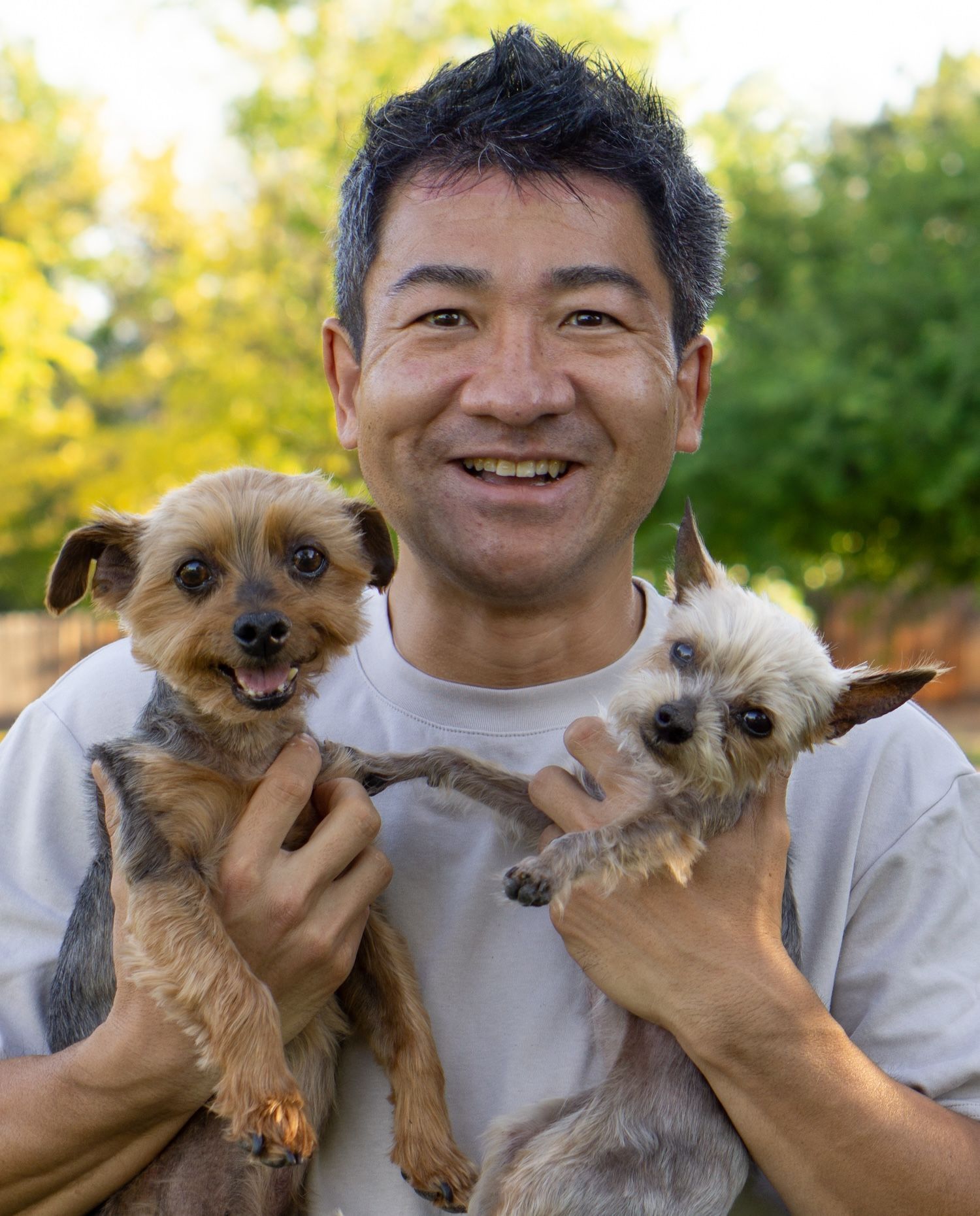 Man holding two small dogs outside, smiling.