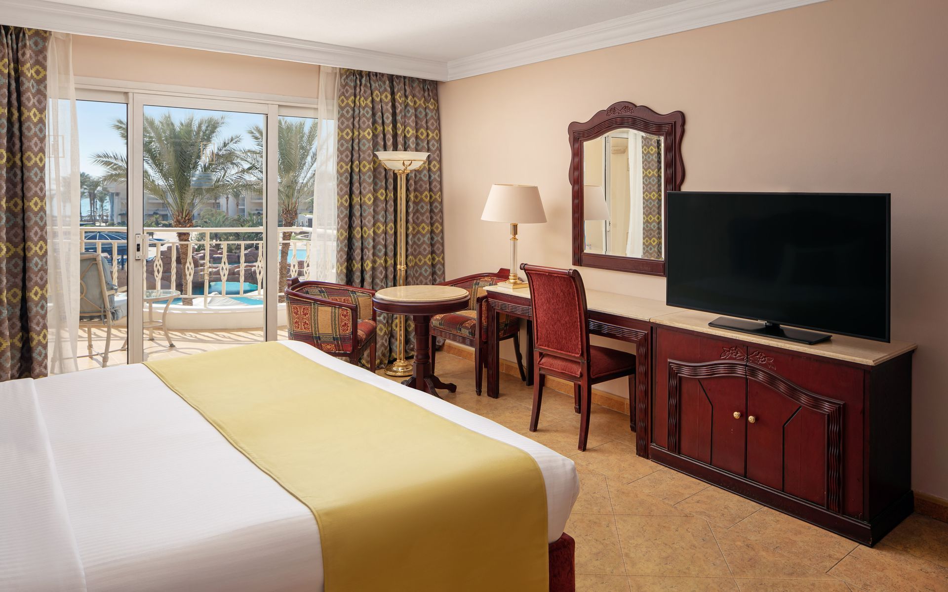 A hotel room with a king size bed , television , desk and chairs.
