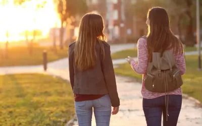 Two young women are walking down a sidewalk at sunset.