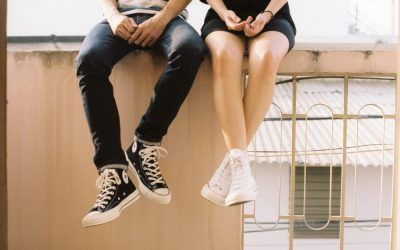 A man and a woman are sitting on a balcony with their legs crossed.