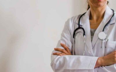 A female doctor with a stethoscope around her neck is standing with her arms crossed.