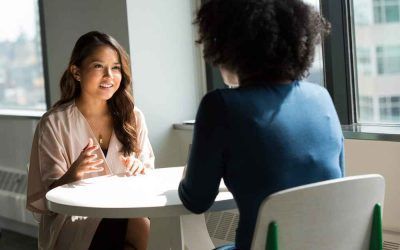 Two women are sitting at a table having a conversation.