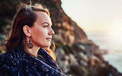 A woman is standing on top of a cliff overlooking the ocean.