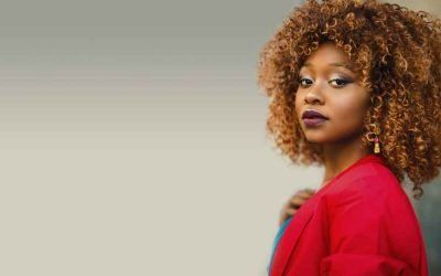 A woman with curly hair is wearing a red jacket and earrings.