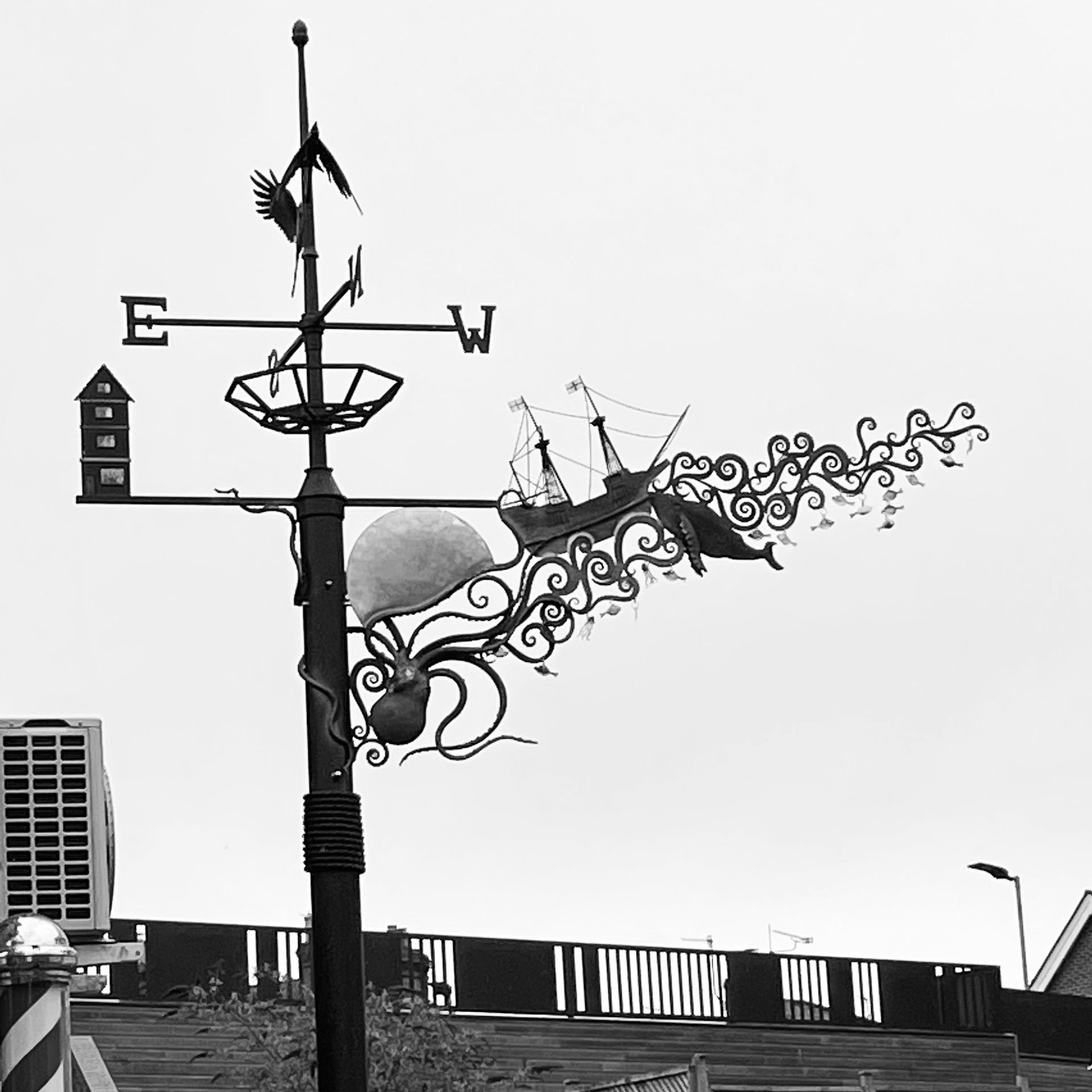 Weather vane with ship, octopus, and birdhouse, atop a black pole.