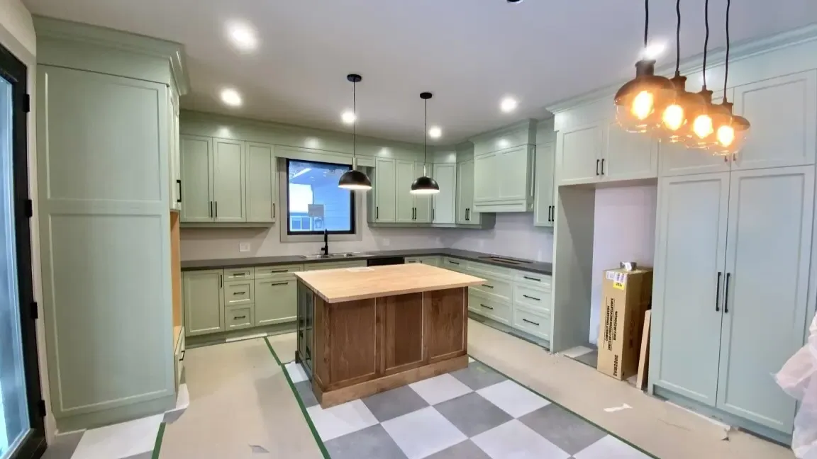 A kitchen under construction featuring light green cabinets, a wood-topped center island, and a checkered floor.