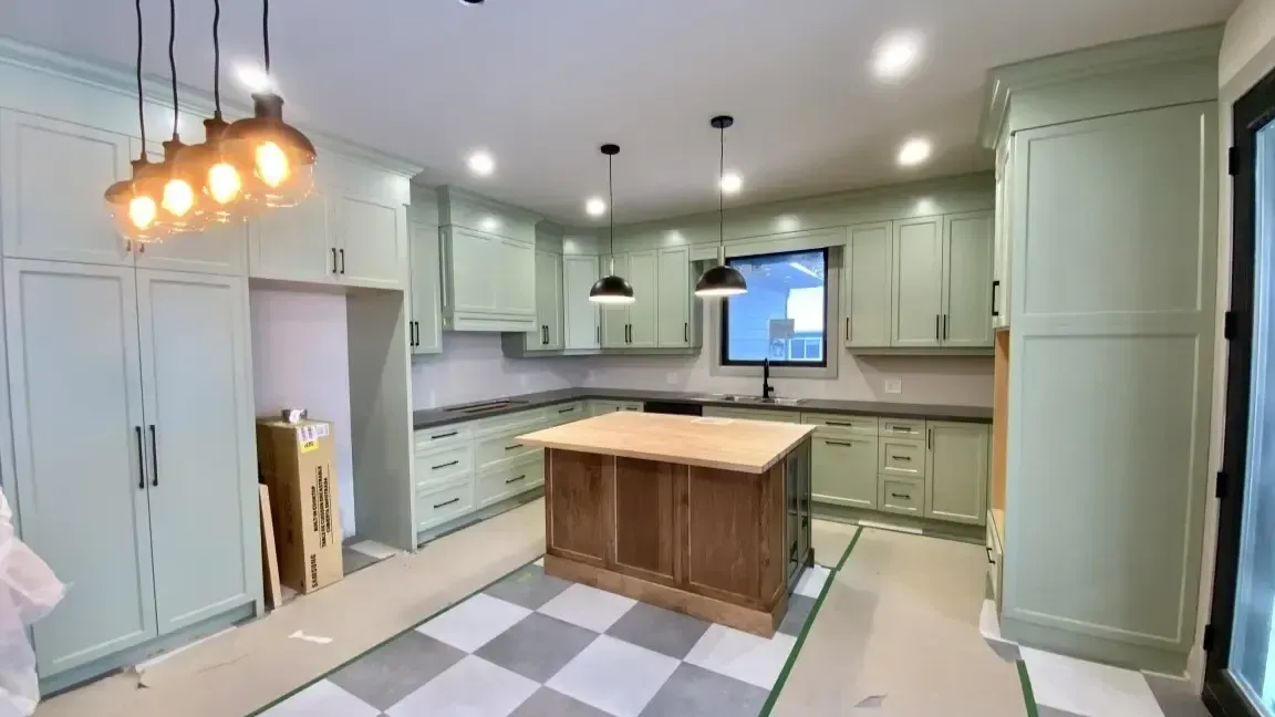 A kitchen under construction featuring light green cabinets, a wood-topped center island, and a checkered floor.