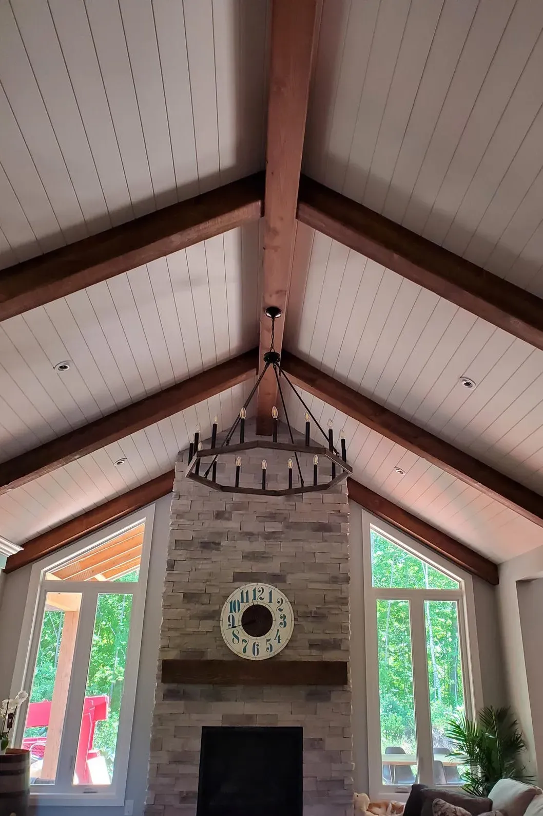 A fireplace with a stone chimney and wooden mantel under vaulted ceilings with exposed beams and a large iron chandelier.