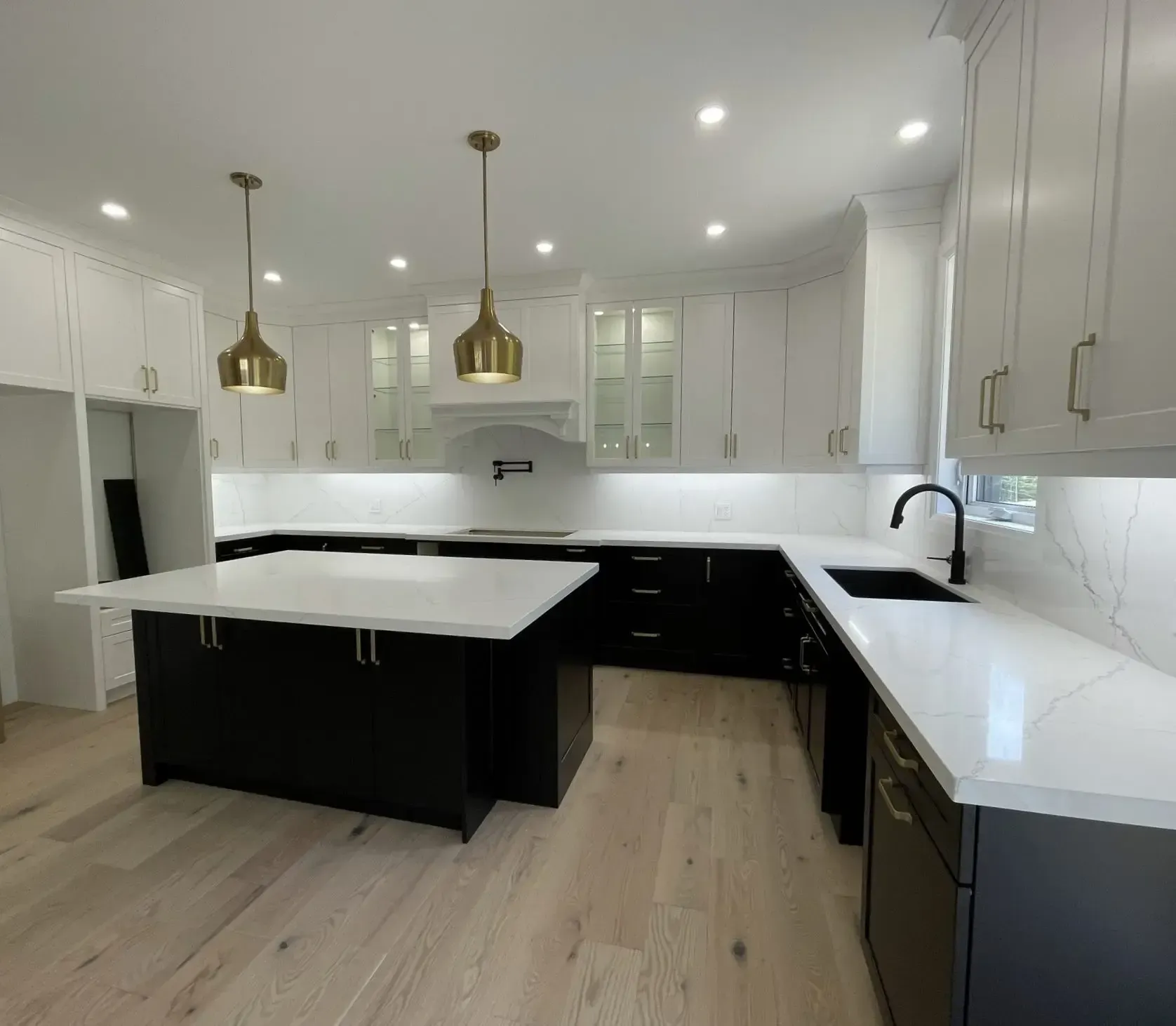 A modern kitchen features white upper cabinets, black lower cabinets, a large central island, and light wood flooring.