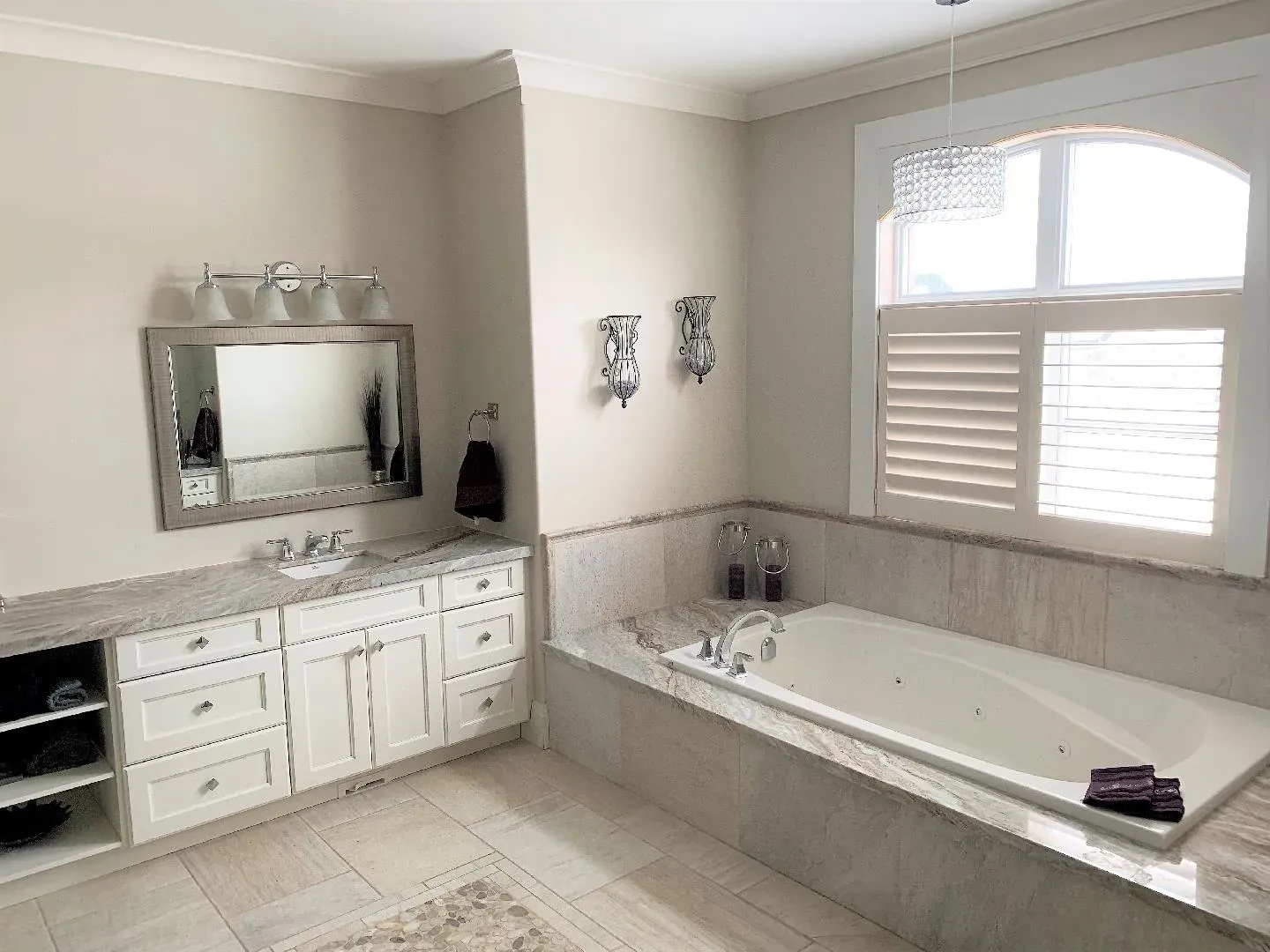 A modern, neutral-toned bathroom featuring a vanity with white cabinets, a large mirror, and a built-in jetted bathtub.