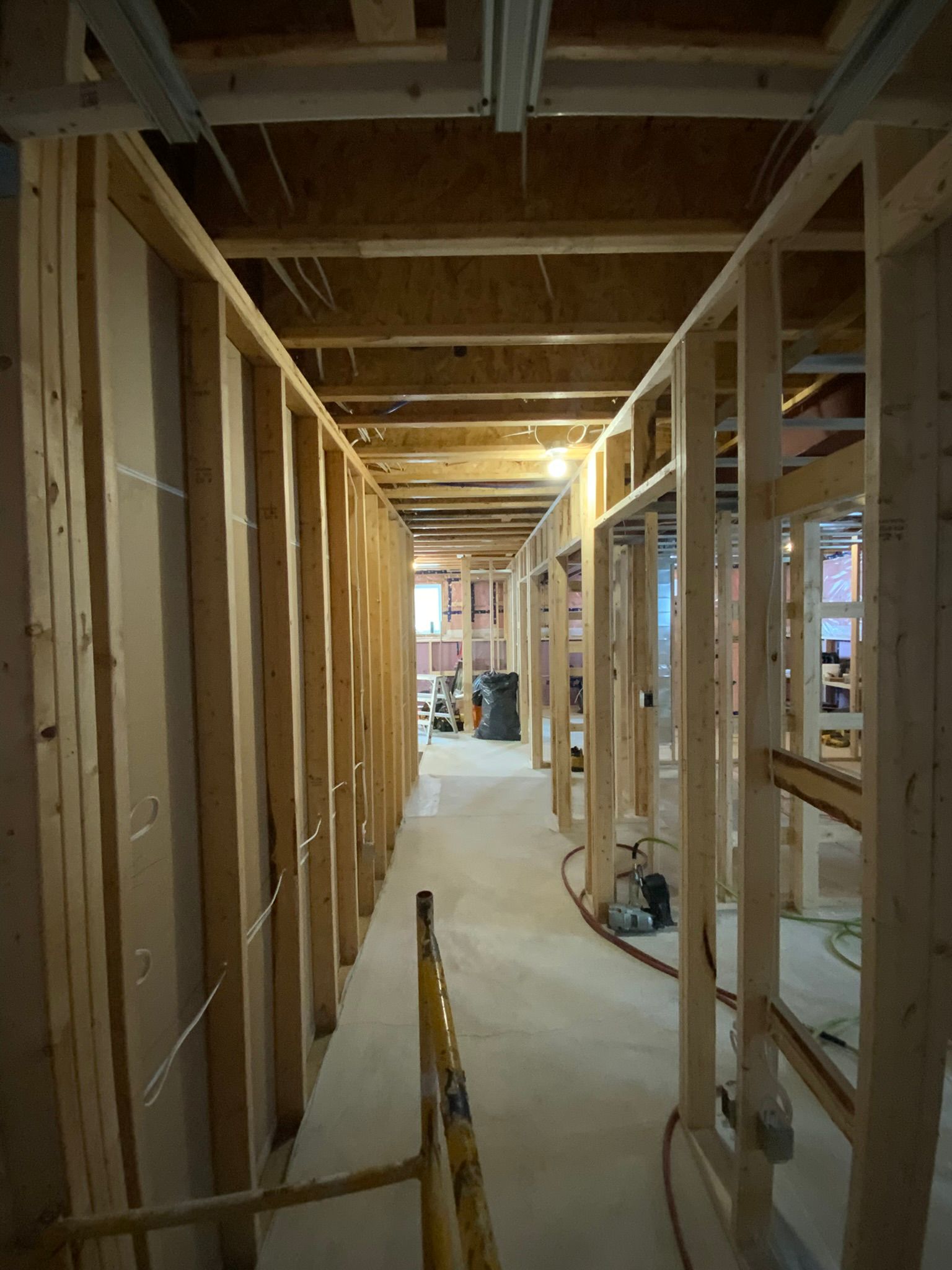 Interior of a framed hallway under construction with exposed wooden studs and a concrete floor