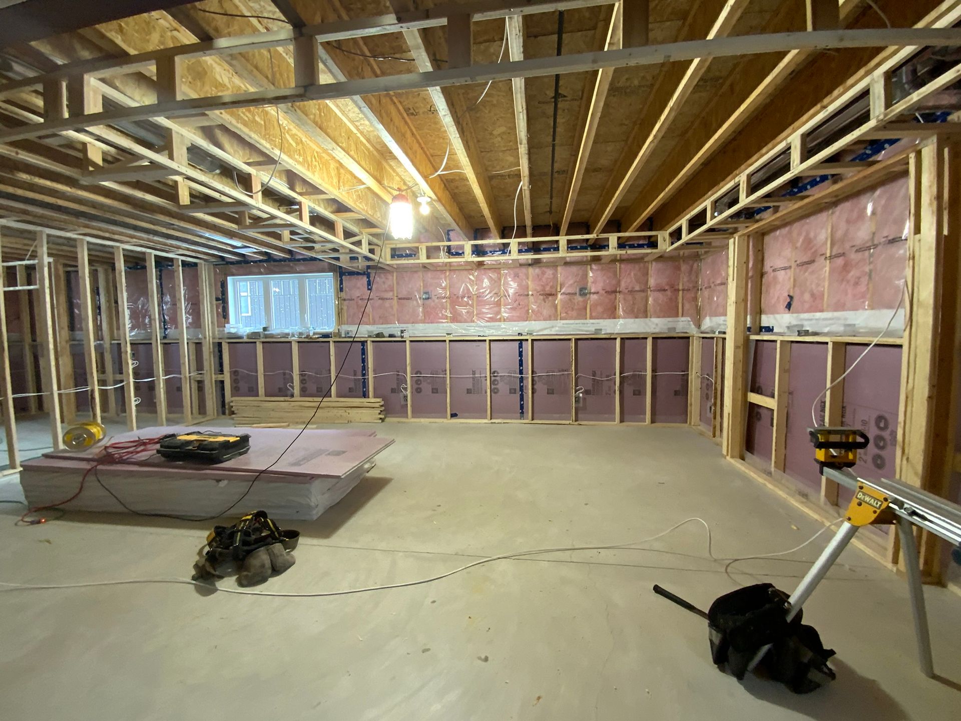 Unfinished basement framing with exposed joists, insulation, and construction tools on the floor.