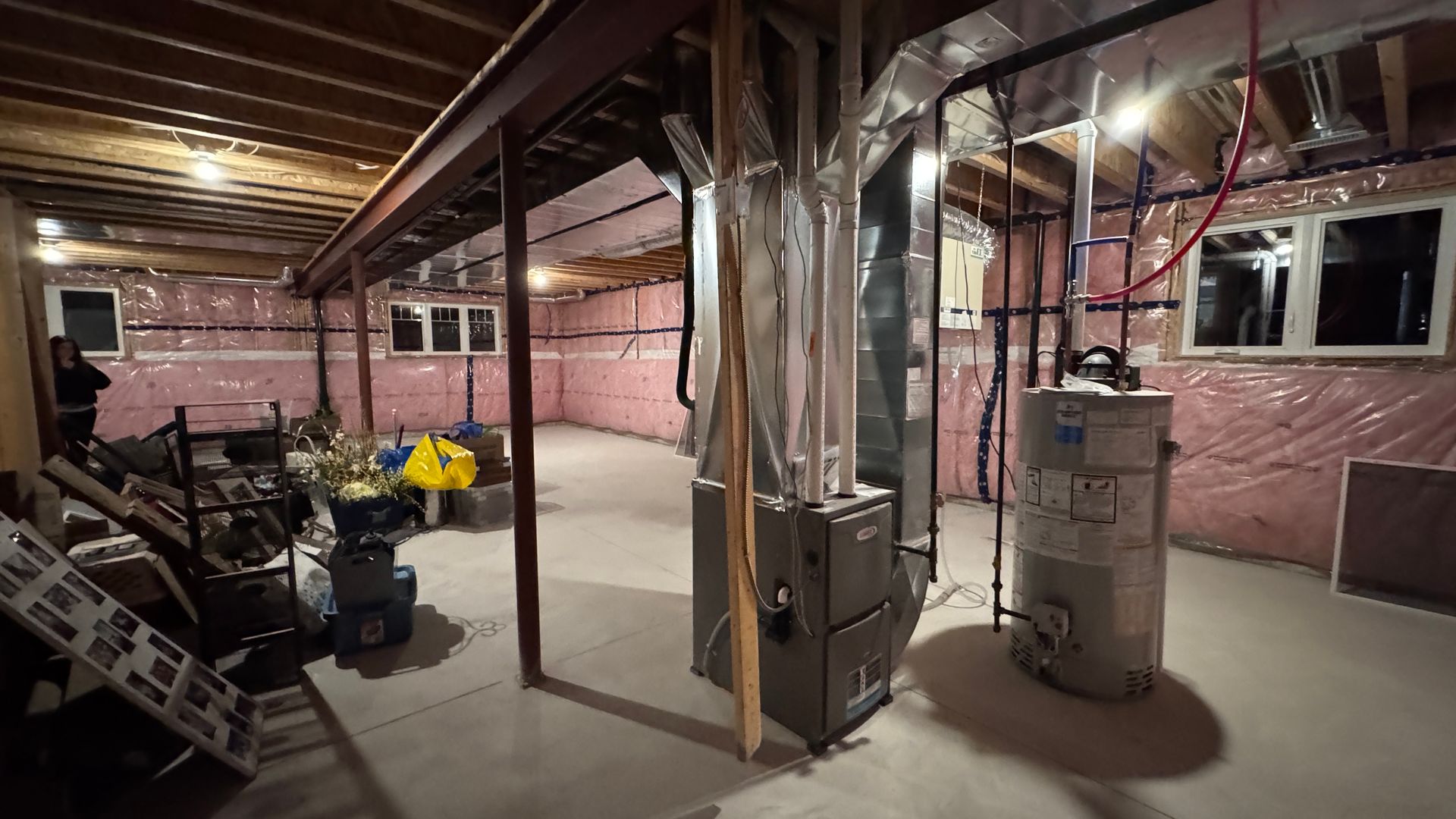 Basement under renovation with exposed insulation, beams, and furnace equipment.