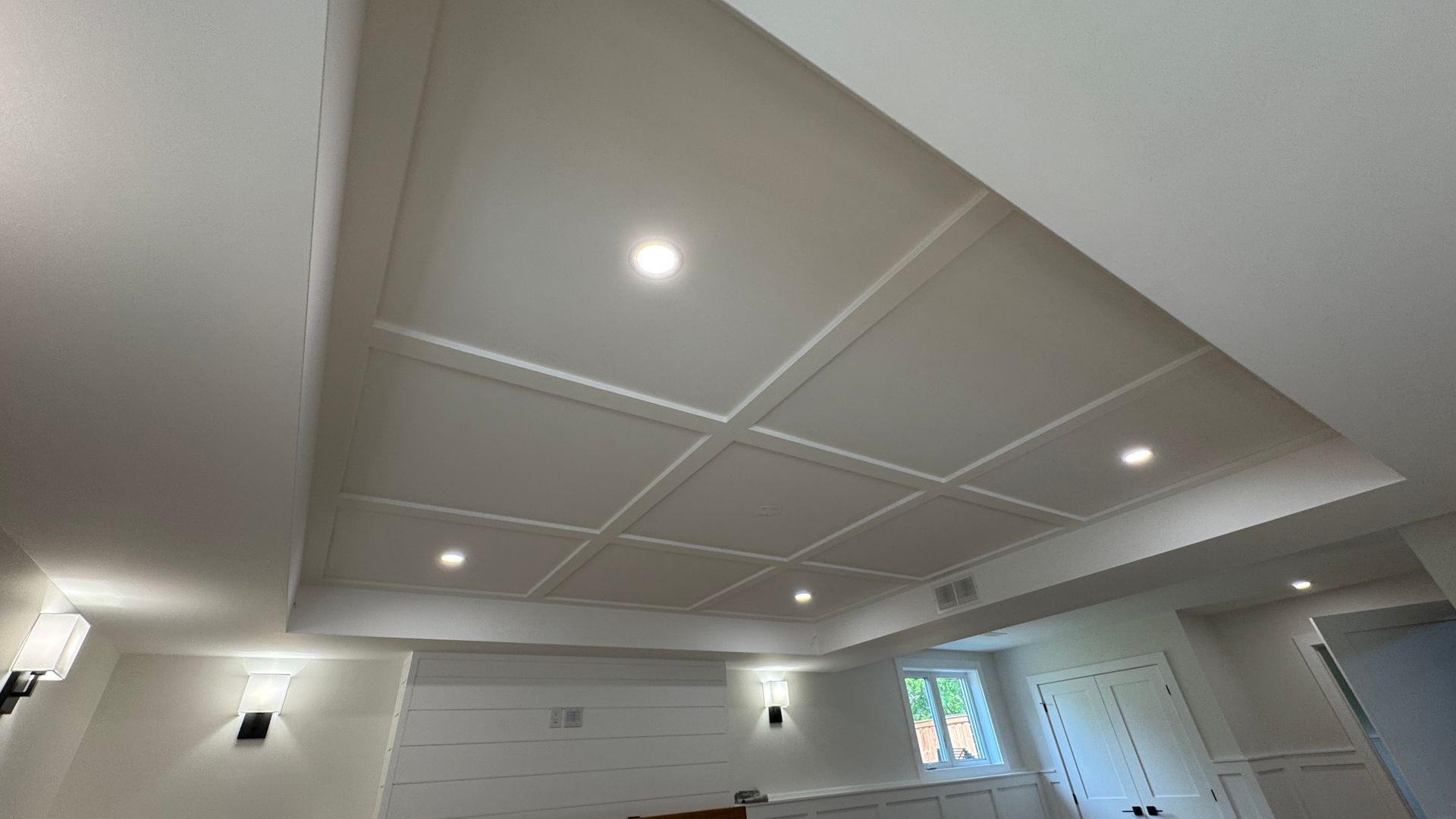 Empty modern room with a recessed tray ceiling, recessed lights, and windows on the right.