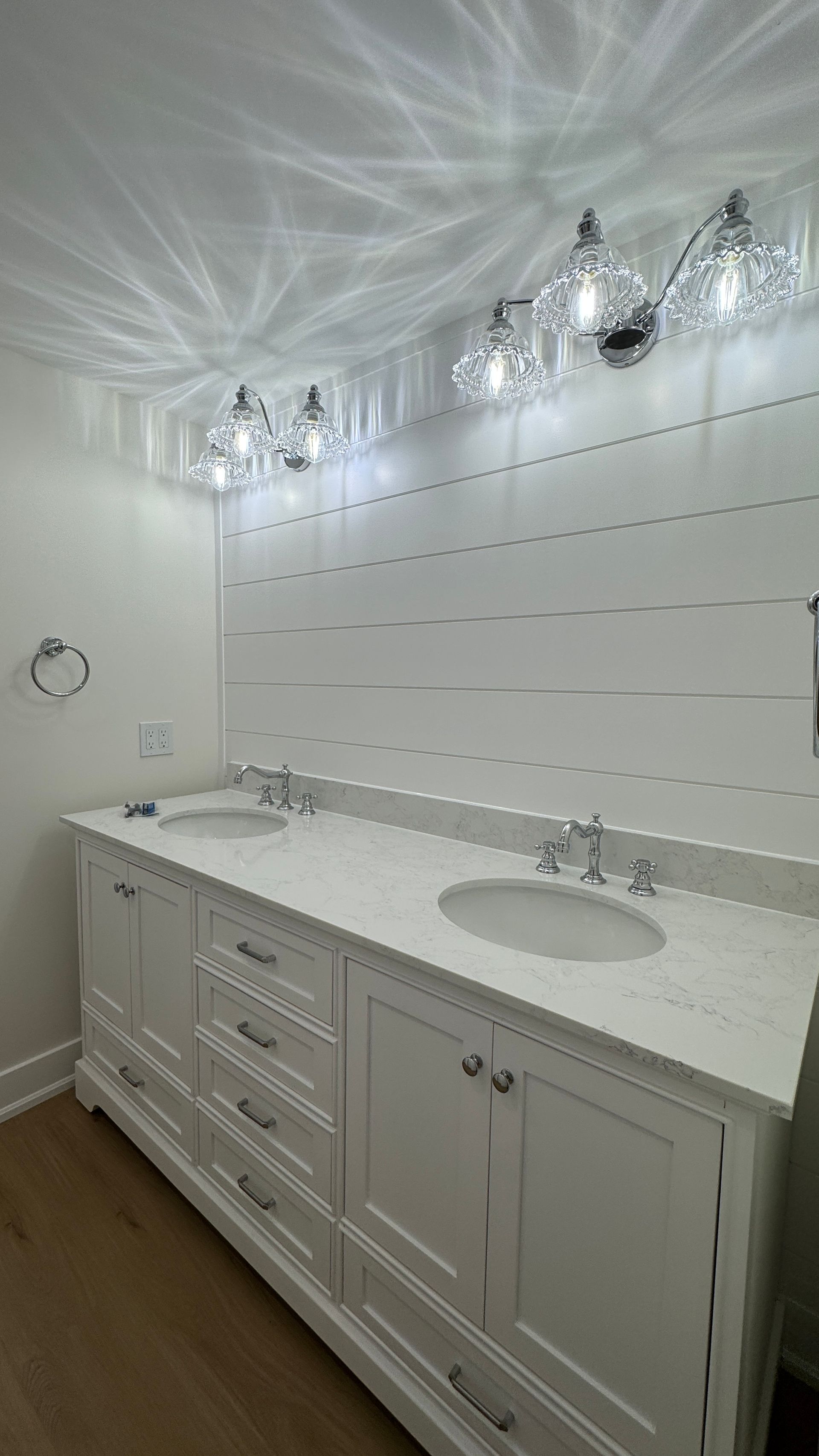 Bright bathroom vanity with white cabinets, double sink, and lit wall sconces over a tiled backsplash