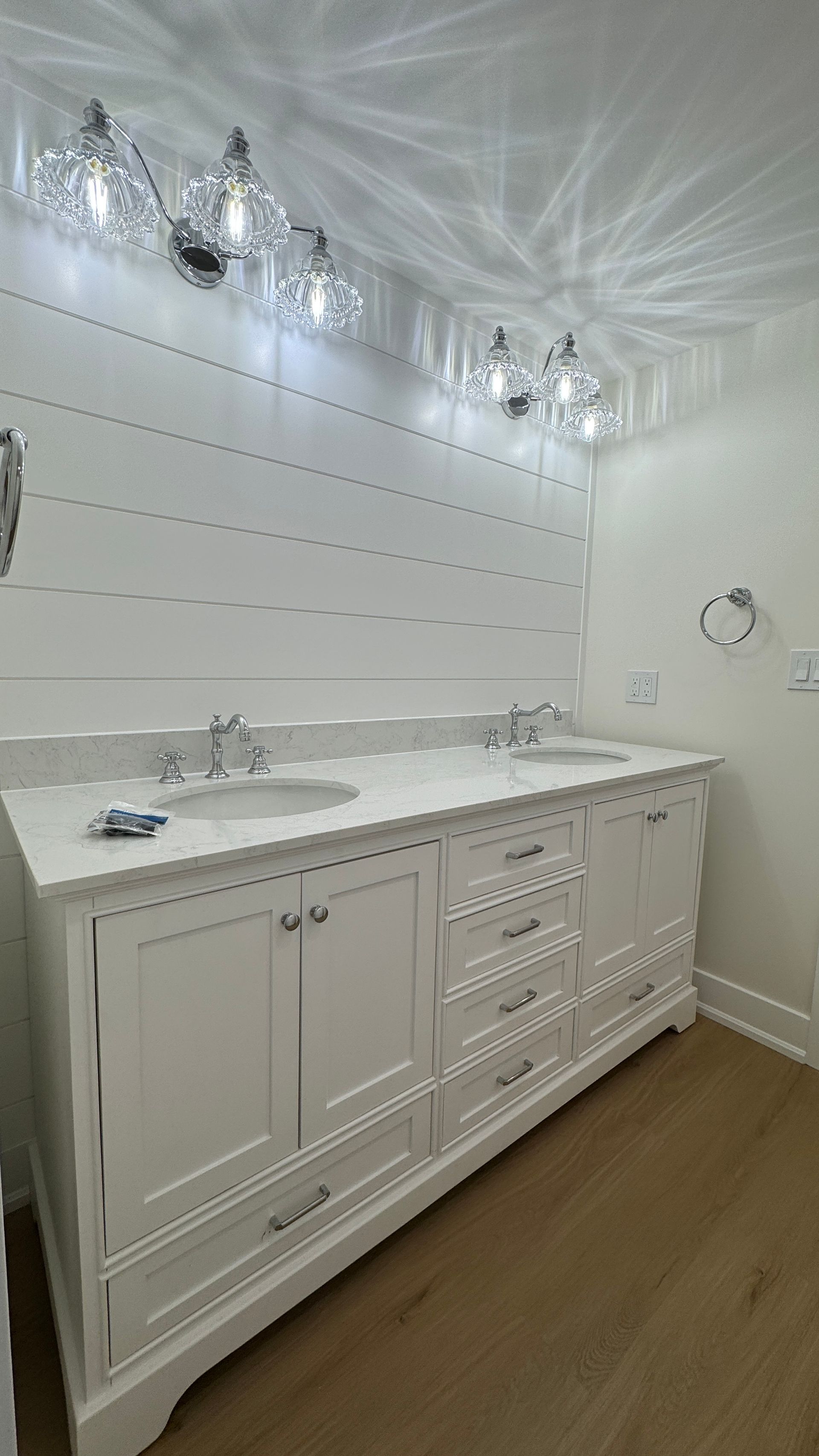 White bathroom vanity with sink, drawers, and lit mirrors against a tiled wall