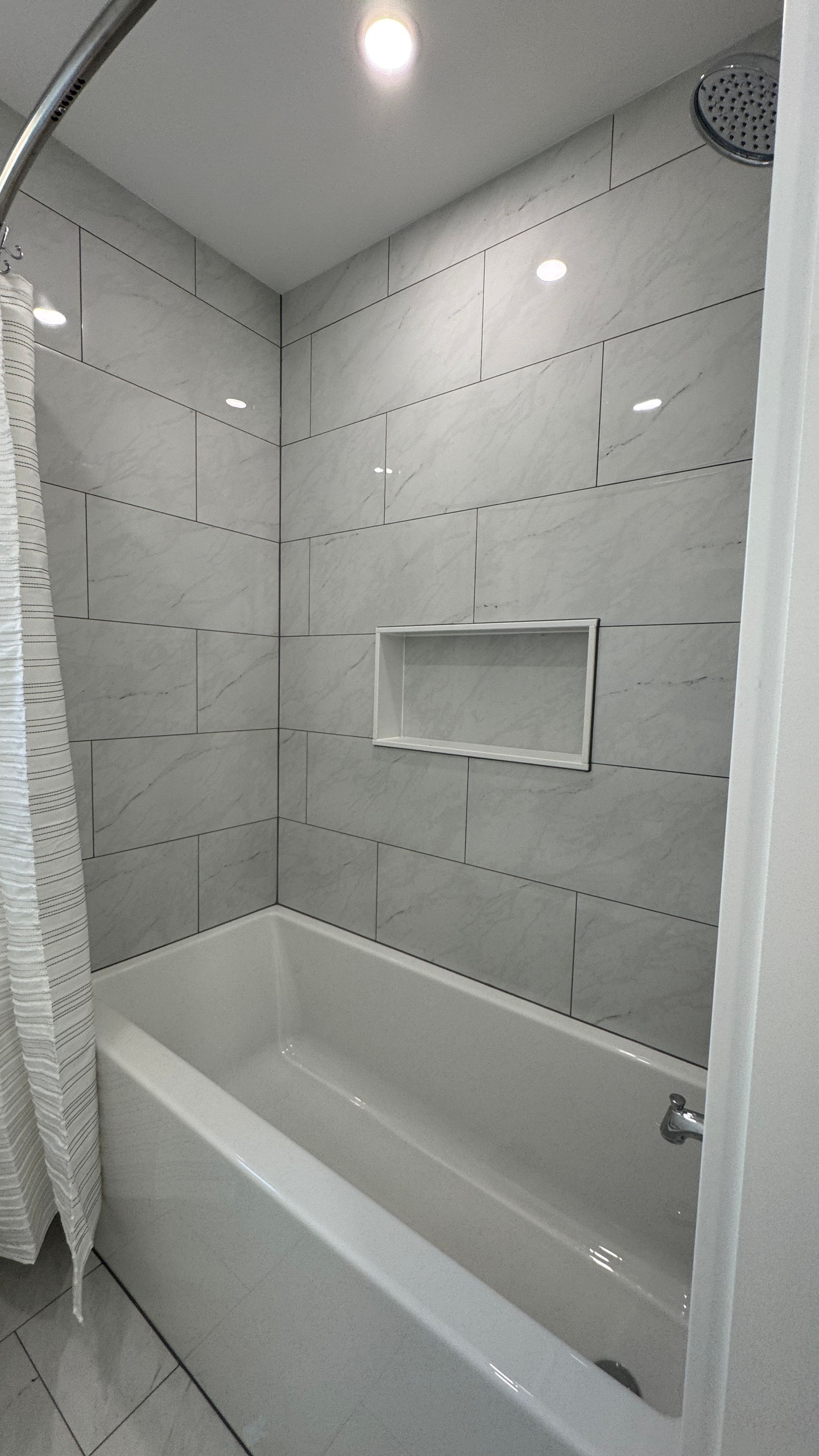 Small tiled bathroom with a white bathtub and built-in shower niche.