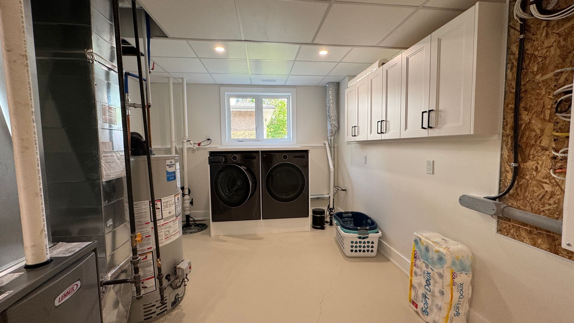 Basement laundry room with washer and dryer, white cabinets, and storage shelves under bright windows