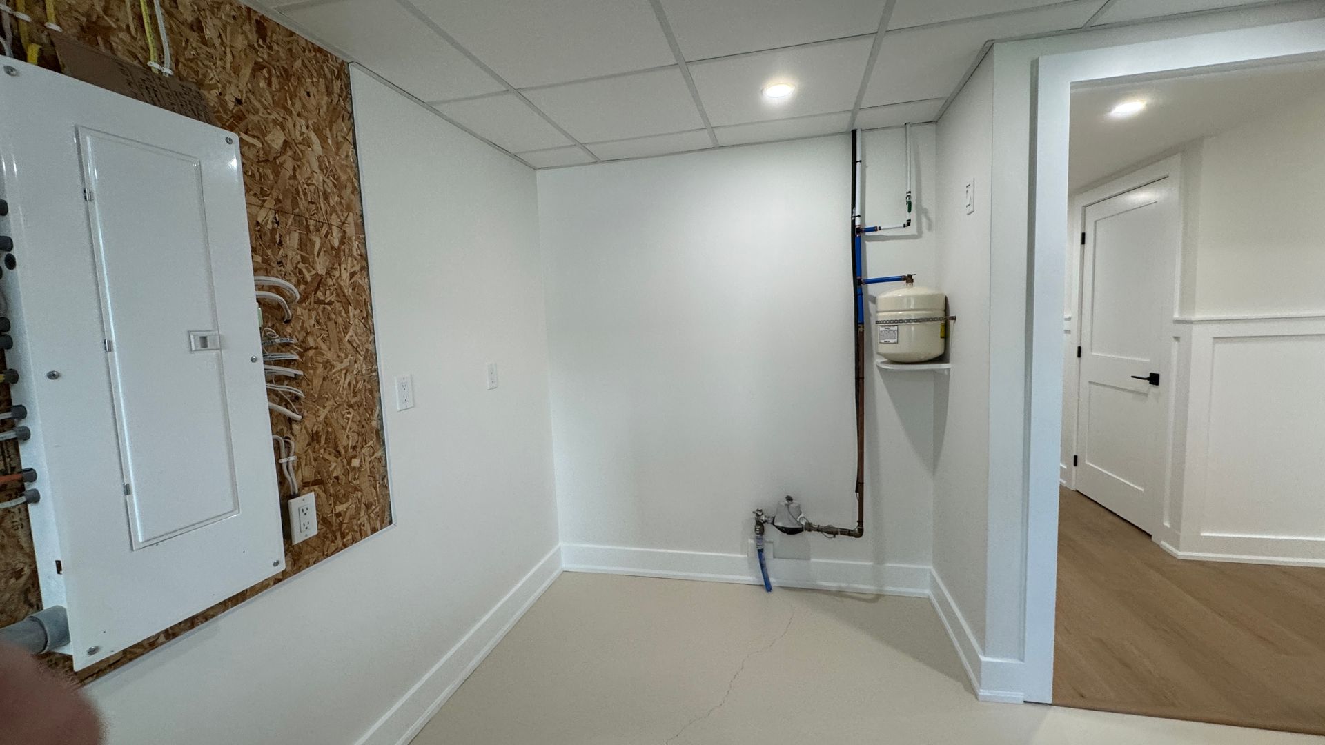 Empty room with white walls, beige carpet, and a doorway to a hall with wood flooring.